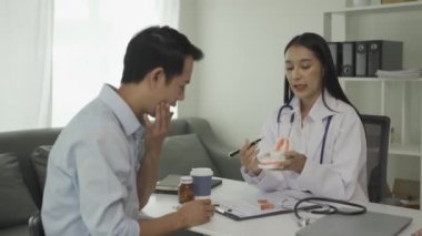 Beyaz laboratuvar önlüğü ve sınav eldivenleriyle gülümseyen güzel kadın dişçi, diş aletleri kullanıyor ve diş sağlığı kliniğinde diş modeli olan genç erkek hastayı muayene etmeye başlıyor..