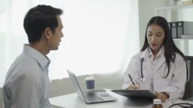 Beyaz üniformalı genç Asyalı doktor sağlık sorunlarını tartışmak için klinikteki erkek hastayla sonuçları ya da belirtileri tartışmak için pano kullanıyor..