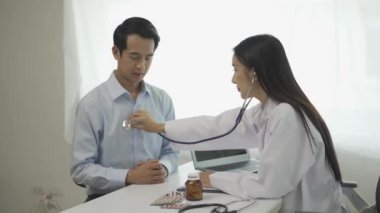 Beyaz üniformalı genç Asyalı doktor sağlık sorunlarını tartışmak için klinikteki erkek hastayla sonuçları ya da belirtileri tartışmak için pano kullanıyor..