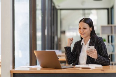 Güzel Asyalı iş kadını mutlu bir şekilde gülümsüyor iş müşterisiyle cep telefonuyla konuşuyor, akıllı telefondan iş birliği içinde buluşuyor.