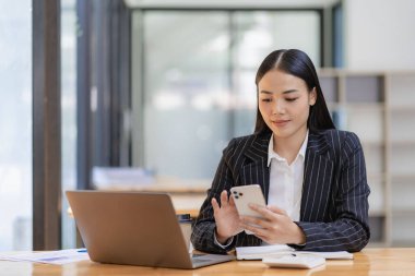 Güzel Asyalı iş kadını mutlu bir şekilde gülümsüyor iş müşterisiyle cep telefonuyla konuşuyor, akıllı telefondan iş birliği içinde buluşuyor.