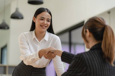 İki Asyalı iş kadını el sıkışıyor ve proje sunum belgesi, pazarlama planı analizi hakkında tartışıyorlar. finansal iş