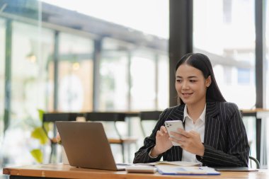 Asyalı iş kadını elinde belgelerle dizüstü bilgisayar kullanıyor. Not defteri masanın üstünde. Rapor analizi planlama finansal istatistikler