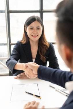 Yeni başvuruları kabul etmekten mutlu olan Asyalı genç bir iş adamıyla el sıkışan bir iş adamının yakın çekimi. Profesyonel bir çalışan, başvuranları ofisteki masada karşılar..