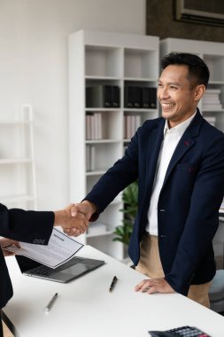 Yeni başvuruları kabul etmekten mutlu olan Asyalı genç bir iş adamıyla el sıkışan bir iş adamının yakın çekimi. Profesyonel bir çalışan, başvuranları ofisteki masada karşılar..