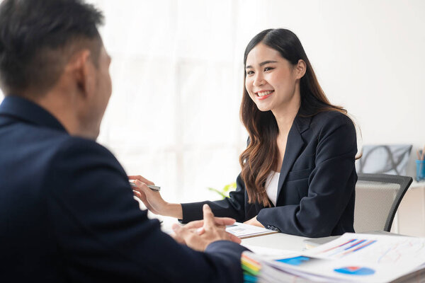 Two Asian business men and women smiling happily working with laptops and financial documents. They talk about their projects and brainstorm creative ideas together in the office.