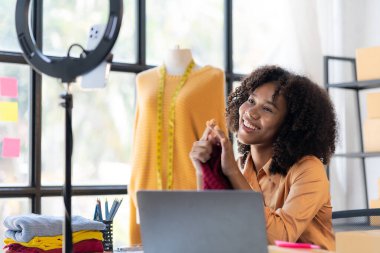 Afrikalı Amerikalı kız internetten canlı yayın yoluyla giysi sunar ve satar, şık bir giyim mağazası seçer. Moda tasarımcıları yeni koleksiyonların resimlerini çiziyor.