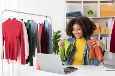 Afrikalı Amerikalı kız internetten canlı yayın yoluyla giysi sunar ve satar, şık bir giyim mağazası seçer. Moda tasarımcıları yeni koleksiyonların resimlerini çiziyor.