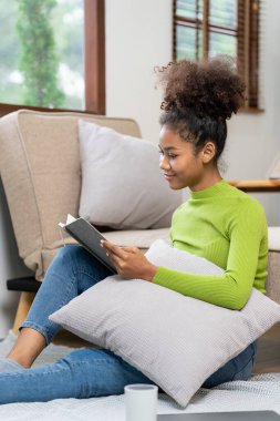 Çekici genç Afrikalı kadın evde boş zamanlarının keyfini çıkarırken evde dizüstü bilgisayarda çalışırken kulaklık takıyor ve akıllı telefon ve tablet kullanıyor..