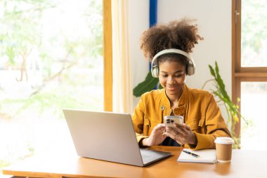 Kafede dizüstü bilgisayarla çalışan genç Afrikalı bir kadın. Millennial Afro-Amerikan kızı. Kulaklığı kafeteryada dizüstü bilgisayarla çalışıyor.