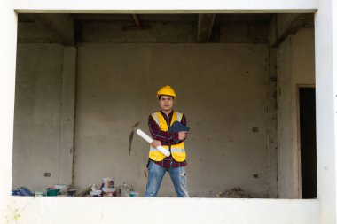 Genç Asyalı mühendis mimariyi, inşaat projesi konseptini, miğfer ve bina inşaatında tasarım kağıdında genç profesyonel mühendisi denetliyor..