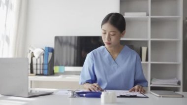 Hastanedeki masasında hasta evrakları üzerinde çalışan genç Asyalı hemşire.