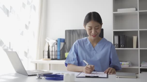 若いアジアの看護師は 病院で一人で彼女の机で患者の文書に取り組んでいます — ストック動画