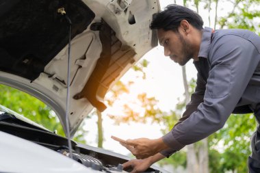 Otomobil tamircisi kontrol ve kontrol listesini panoya yazarak arabayı teftiş eder. Tamirci dizüstü bilgisayardaki araba parçaları stoğunu kontrol ediyor ve yol kenarındaki araba bozulmuş.