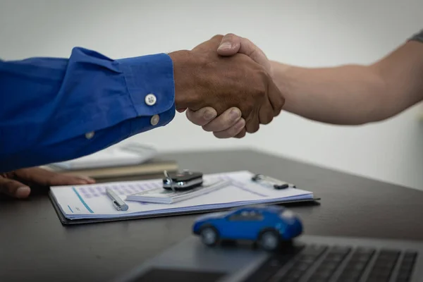Close-up of a salesperson shaking hands with a man in the sales office after the successful signing of the contract and payment. A car dealer or sales manager offers to sell a car.