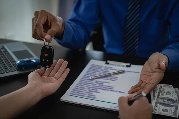 Vehicle rental business concept Close up of hands of car rental agent giving car remote key to customer after signing contract on table, sales and insurance concept