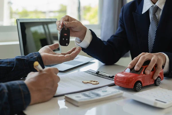 Vehicle rental business concept Close up of hands of car rental agent giving car remote key to customer after signing contract on table, sales and insurance concept
