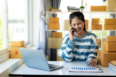 Başarılı bir iş kadını, internet üzerinden satış yaparken ve ev ofisinde paket teslimatı yaparken eğleniyor. Kadın, dizüstü bilgisayar ve KOBİ iş konseptini kontrol ediyor.
