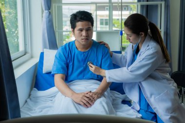 Asyalı erkek hasta, tıbbi sağlık konseptinin yanında danışmanlık ve yardım sağlayan doktor ekibiyle yatakta yatıyor..