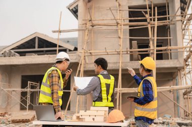 Mimarlar şantiyesindeki mimarlık projelerini tartışan iş arkadaşları inşaat projesi taslağı ve mimari planı için Mühendis ile birlikte inceleme sahasında çalışıyorlar.
