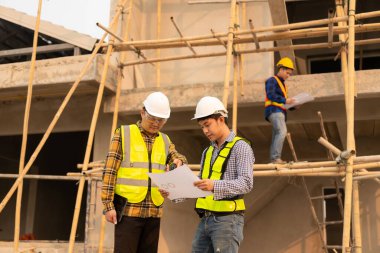 Mimarlar şantiyesindeki mimarlık projelerini tartışan iş arkadaşları inşaat projesi taslağı ve mimari planı için Mühendis ile birlikte inceleme sahasında çalışıyorlar.