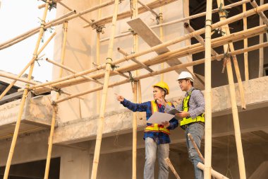 Mimarlar şantiyesindeki mimarlık projelerini tartışan iş arkadaşları inşaat projesi taslağı ve mimari planı için Mühendis ile birlikte inceleme sahasında çalışıyorlar.