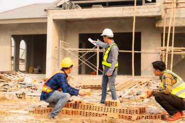 Mimarlar şantiyesindeki mimarlık projelerini tartışan iş arkadaşları inşaat projesi taslağı ve mimari planı için Mühendis ile birlikte inceleme sahasında çalışıyorlar.