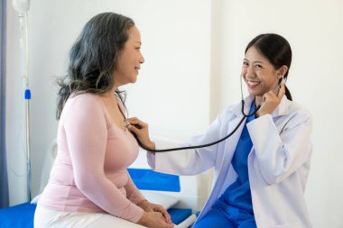 Asyalı kadın doktor, hastanede hastayı cesaretlendirmek için gülümseyen bir hastayla konuşuyor. Yaşlı bir Asyalı kadın, hastane ofisindeki bir doktoru ziyaret ediyor. Sağlık muayenesinin sonuçları hakkında konuşalım.