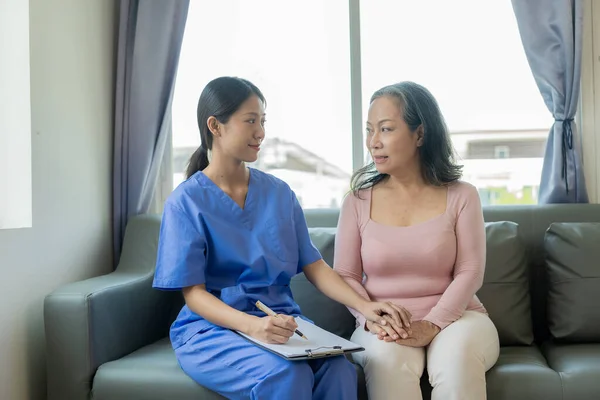 Asian female doctor talks to patient with smile to encourage patient at hospital An elderly Asian woman visits a doctor at a hospital office. Talk about the results of the health examination
