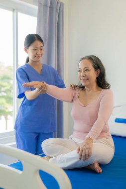 Asyalı kadın fizyoterapisti olan yaşlı bir kadın hasta. Kolunu fizik tedavi için tutuyor. Zayıf kasları tedavi ediyor. Hastanenin muayene odasında bu egzersizi yapmaya niyetli bir hasta görülüyor..