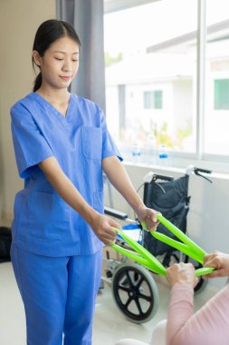 Asyalı kadın fizyoterapisti olan yaşlı bir kadın hasta. Kolunu fizik tedavi için tutuyor. Zayıf kasları tedavi ediyor. Hastanenin muayene odasında bu egzersizi yapmaya niyetli bir hasta görülüyor..