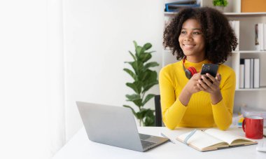 Kulaklık takan, akıllı telefon takan, bilgisayar ekranına bakan, web kamerasıyla görüntülü sohbet yapan, online iş konsepti olan genç Afrikalı Amerikalı kız..