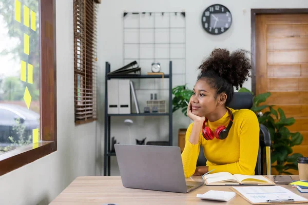 Young African American girl wearing headphones, smartphone, video call on laptop, looking at computer screen, watching webinar or doing video chat by webcam, online work concept.