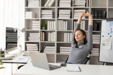 Ofisteki işinde mutlu genç bir kadın. Rahatlatıcı. Ellerini uzatıyordu. Tatmin olmuş, rahat bir iş kadını. Elleri kafasında bir sandalyede oturuyor. Ofisteki yeni işinden zevk alıyor..