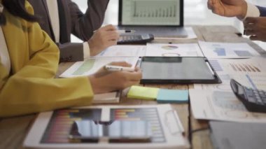 Takım elbiseli bir grup Asyalı genç iş adamı bir iş toplantısında beyin fırtınası yapıyorlar. Grafik belgeleri ve dizüstü bilgisayarlarla planlama, strateji, yeni iş geliştirme.