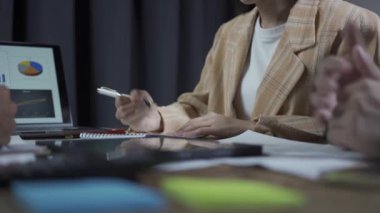 Takım elbiseli bir grup Asyalı genç iş adamı bir iş toplantısında beyin fırtınası yapıyorlar. Grafik belgeleri ve dizüstü bilgisayarlarla planlama, strateji, yeni iş geliştirme.