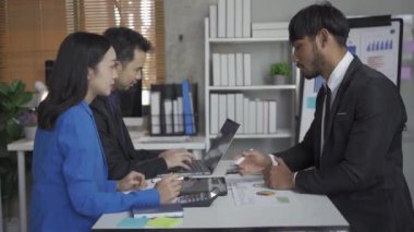 Takım elbiseli bir grup Asyalı genç iş adamı bir iş toplantısında beyin fırtınası yapıyorlar. Grafik belgeleri ve dizüstü bilgisayarlarla planlama, strateji, yeni iş geliştirme.