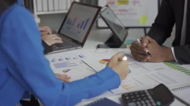 Takım elbiseli bir grup Asyalı genç iş adamı bir iş toplantısında beyin fırtınası yapıyorlar. Grafik belgeleri ve dizüstü bilgisayarlarla planlama, strateji, yeni iş geliştirme.