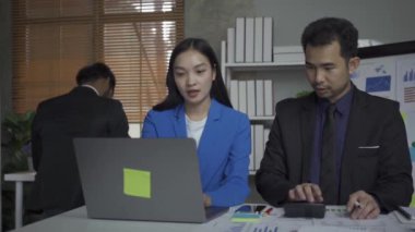 Takım elbiseli bir grup Asyalı genç iş adamı bir iş toplantısında beyin fırtınası yapıyorlar. Grafik belgeleri ve dizüstü bilgisayarlarla planlama, strateji, yeni iş geliştirme.