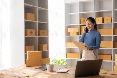 Müşteriyle akıllı telefondan konuşan Asyalı kadın, dizüstü bilgisayar, küçük işletme, e-ticaret ve çevrimiçi alışveriş, küçük ve yeni girişimci, perakende sektörü, KOBİ
