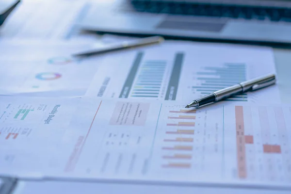 Rapor sayfası, malzemeler ve düz bilgisayar olan ofis masası. Ofisteki tabloda finansal grafik verileri ile