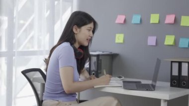 Kulaklık takan genç Asyalı kız öğrenci online ders alırken ya da konferans verirken internette geziniyor ve Google Zoom videosu çekiyor.
