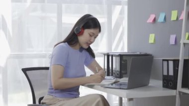Kulaklık takan genç Asyalı kız öğrenci online ders alırken ya da konferans verirken internette geziniyor ve Google Zoom videosu çekiyor.