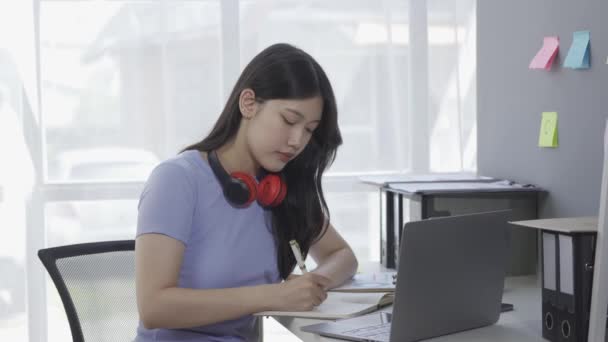年轻的亚洲女学生带着耳机 一边参加在线课程或讲座 一边用笔记本电脑上网 一边用Google Zoom视频通话 — 图库视频影像