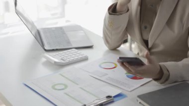 Tasarruf veya muhasebe konseptini hesaplamak için hesap makinesi kullanan genç ve güzel Asyalı muhasebeci dizüstü bilgisayar ve vergi, ticari, araştırma ve muhasebe belgelerinin kopyalarını yapıyor..