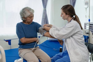 Elinde dosya olan kadın doktor hastanede yaşlı kadın hastayla konuşuyor. Yaşlı kadın ya da dijital tabletli doktor. Kadın hastalarla tıbbi uzmanları tedavi etmek için danışmanlık yapıyor ya da plan yapıyor..