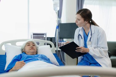 Elinde dosya olan kadın doktor hastanede yaşlı kadın hastayla konuşuyor. Yaşlı kadın ya da dijital tabletli doktor. Kadın hastalarla tıbbi uzmanları tedavi etmek için danışmanlık yapıyor ya da plan yapıyor..