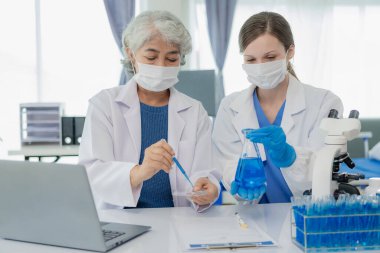 Güzel genç kadın bilim adamı ve iki yaşlı kadın sağlık sektöründe mavi kimyasalları araştıran test tüpleriyle laboratuarda çalışıyorlar..