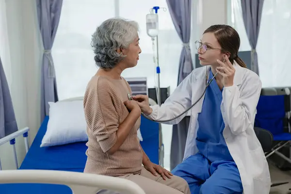 年轻的护士长用听诊器检查心跳 年长的女人 可爱可爱的护士坐在椅子上检查病人 用听诊器和保健概念 — 图库照片