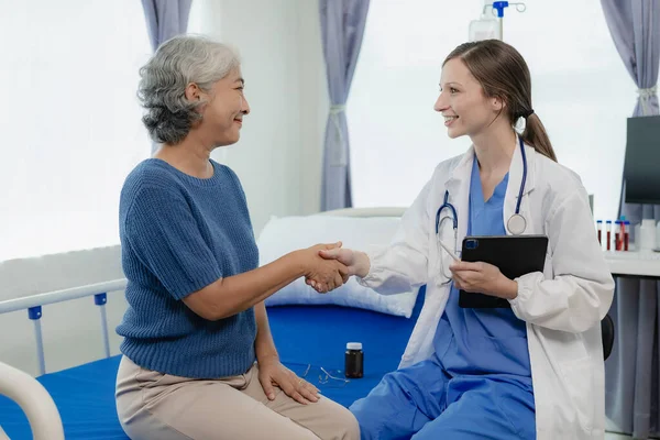 Güzel hemşire hastanede kıdemli bir hastayla el sıkışırken sağlık kayıtlarını tutuyor. Kliniği ziyaret ettikten sonra doktorla tokalaşırken gülümseyen kadın tedaviyi gördüğü için çok minnettar..